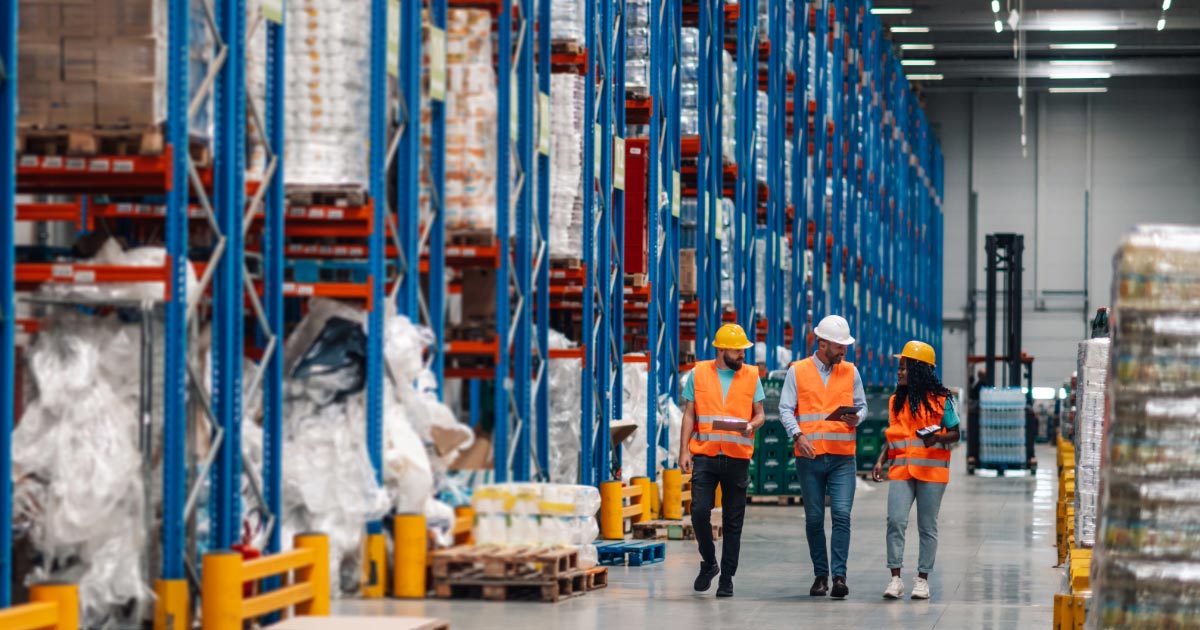 3 warehouse workers wearing safety gear walking by shelves with merchandise
