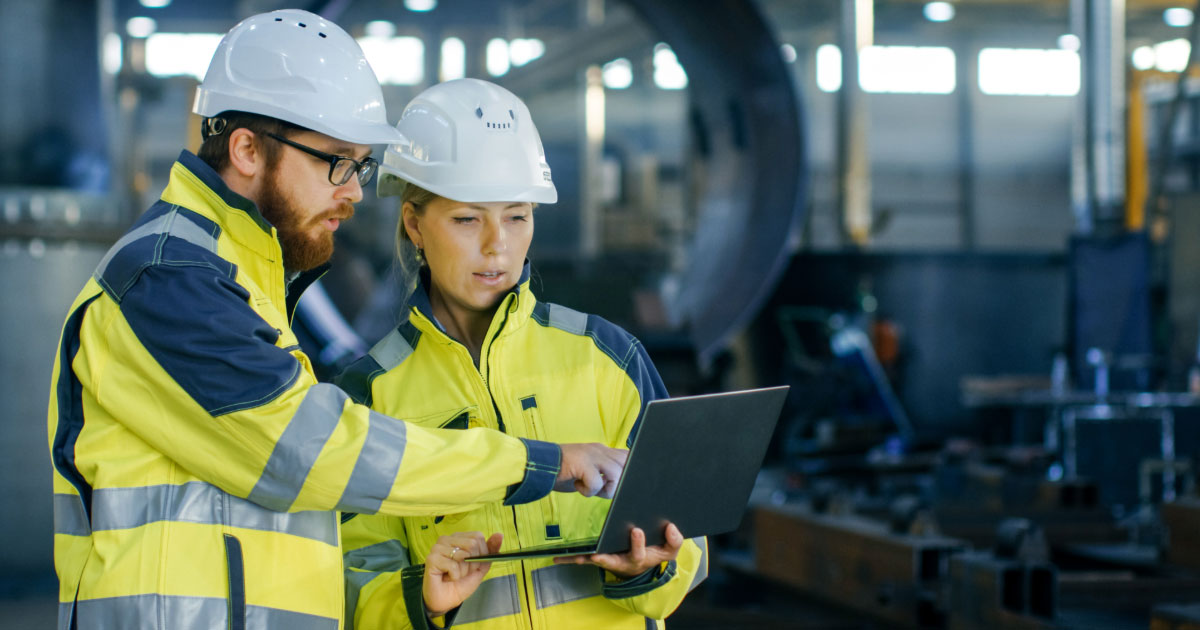 Smiling electrician fixing electric cable on ceiling Two industrial plant workers wearing safety jackets and hardhats looking at laptop