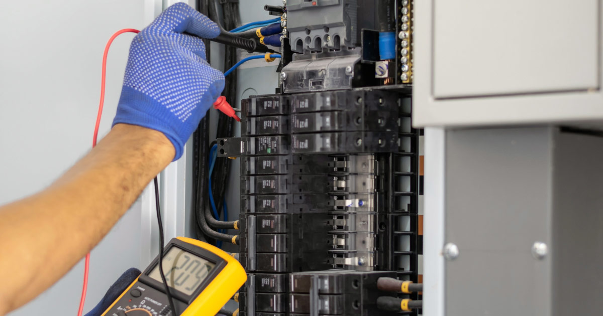 Electrician checking wires in a fuse box with an amp reader