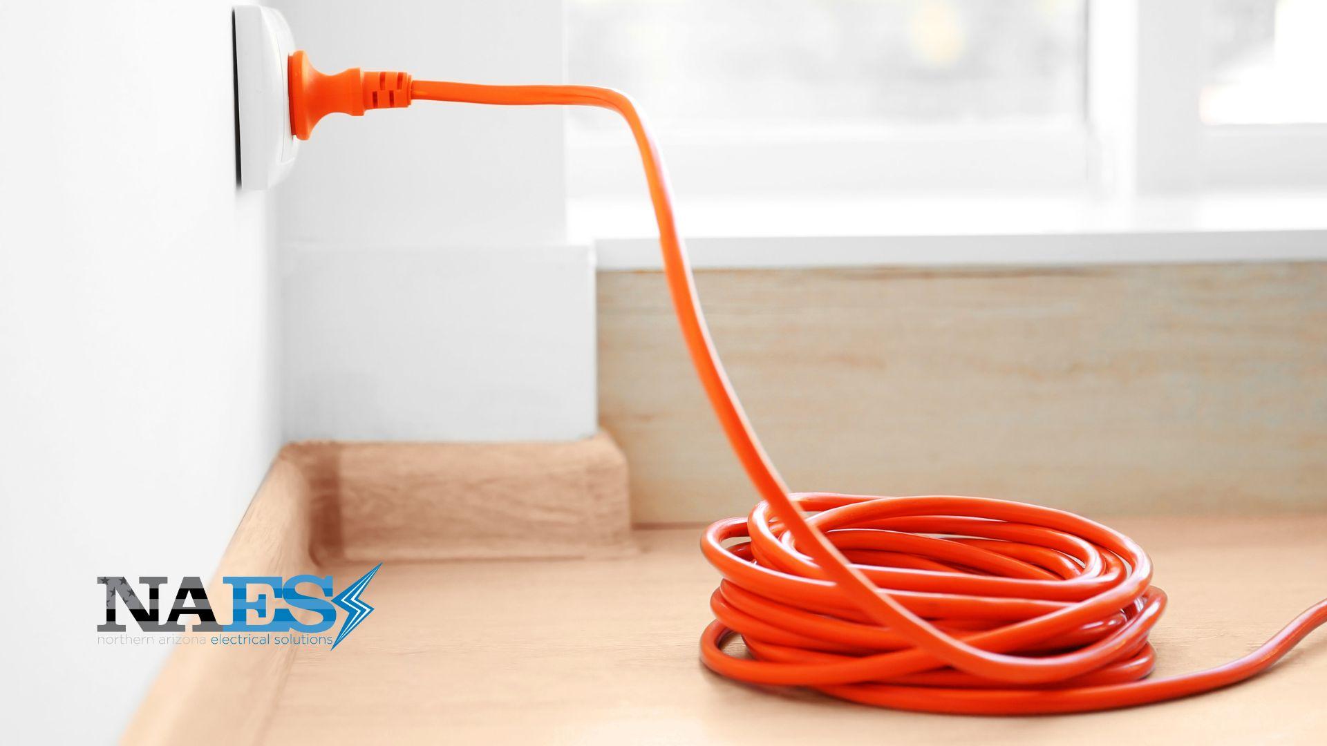 Orange extension cord plugged into a wall outlet as an example of unsafe long-term extension cord use